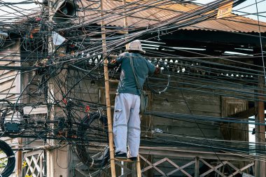 Elektrikçi, eski bir ahşap köyde elektrik sistemini onarmak için merdivenin üzerinde duruyor. Elektrik direklerine bağlı fiber optik kablolar için merdivende çalışan teknisyen..