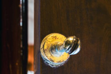 Old brass Door Stopper with brown wooden door and wall. Brass magnetic door stop. Rusty golden Door Stopper or Magnets hold the door. Old classic brass door stopper attached to a dark wooden surface.