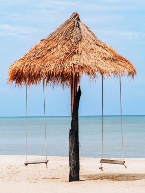 Sahilde tahta salıncak. Plajda rahatlatıcı, huzurlu bir tatil sahnesi. Eski ahşap salıncak güzel deniz ve gökyüzü mavi, deniz tarafından dinleniyor. Tropikal tatil ve tatil beldesi. Tahta ip sallanıyor..