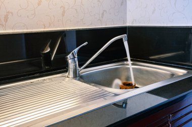 Paslanmaz çelik mutfak lavabosunda lavabo musluğu olan seramik kahve fincanı. Sulu kahve fincanı. Musluğu açarak temiz kahve fincanı. İçinden su akmasına izin vererek..
