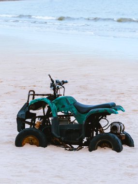 Kumsalda eski model yeşil ATV. Sahilde park halindeki tüm arazi araçları, motorlu bisikletler, parlak bir günde yaz güneşinin parlamasıyla harekete geçmeye hazır. Açık havada aşırı adrenalin sporu.