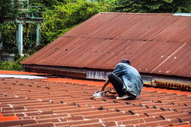 Teknisyen çatıdaki sızıntıyı kapatmak için poliüretan kullanıyor. Adam yağmur sızıntılarını kapatmak için dolgu macunu sürerek çatıyı onardı. İşçi eski kiremit çatısını onarmak için su geçirmez çatı kaplaması kullanıyor..