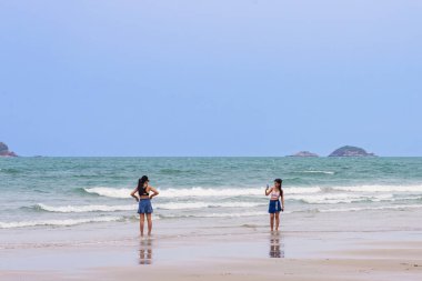 HUA HIN, THAILAND-MARCH 9.2024: Kimliği belirsiz genç, kaygısız kadın arkadaşlarının cep telefonu kullanmaları ve Hua Hin plajında fotoğraf çekmeleri. Seyahat, turizm ve tatil kavramı.