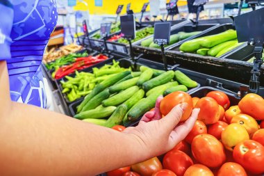 Süpermarkette domates seçen kadın müşterilerin eli. Pazarda elinde domates olan bir kadın. Sağlıklı yaşam tarzı kavramı. Bulanık arka planda olgunlaşmış domates. Marketten olgun domates seç.