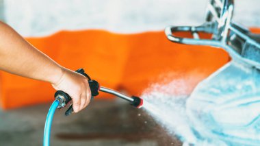 Otomatik para ile çalışan oto yıkama makinesinde motosikletini ya da motosikletini yıkayan mutlu bir kadın. Su ve köpükle oto yıkamada motosiklet temizlemek. Ellere seçici odaklanma.