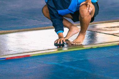 Erkek sporcu asistanı, römorkör yarışmasından önce kaymayı önlemek için temizlik solüsyonu ve havluyla savaş alanının zeminini siliyor. Kaymayı ve düşmeyi önlemek için temizleme.