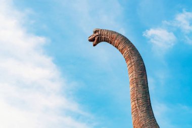 Toy Dinosaur head. Dinosaur head on sky background. View of a dinosaur head sculpture against blue sky. Brachiosaurus with blue sky background. A long necked brachiosaurus head in the forest sky. clipart