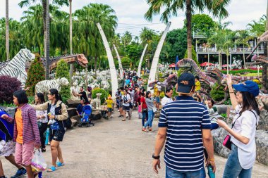 PATTAYA, THAILAND-Aralık 30. 2018: Nong Nooch Tropik Botanik Bahçesi 'ndeki canlı benzeri manzaraya karşı heykelleri veya çeşitli gerçekçi dinozor heykelleri olan tanımlanamayan turistler