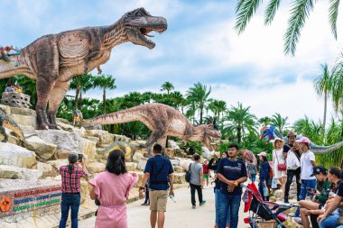 PATTAYA, THAILAND-Aralık 30. 2018: Nong Nooch Tropik Botanik Bahçesi 'ndeki canlı benzeri manzaraya karşı heykelleri veya çeşitli gerçekçi dinozor heykelleri olan tanımlanamayan turistler