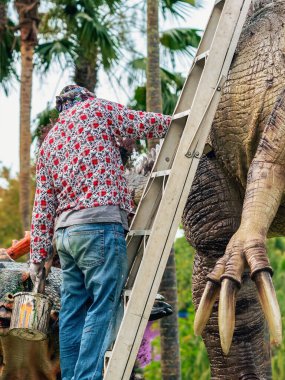 PATTAYA, THAILAND-Aralık 30. 2018: Ressam, Nong Nooch Tropik Botanik Bahçesi 'ni güzel ve gerçekçi kılmak için büyük dinozor heykeli veya heykelini boyamak ve dekore etmek üzere merdivenin üzerinde duruyor.