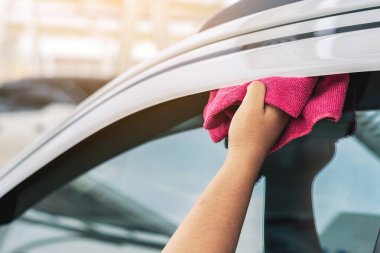 Genç bir kadının eli, pencere saptırıcısının ya da beyaz renkli rüzgar saptırıcılarının içinde pembe bir bez ve mendil tutuyor. Araba temizliği. Pembe bir araba temizleyicisi tutan bir kadın. Temiz araba penceresi kavramı.