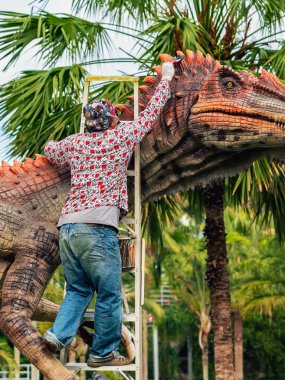 PATTAYA, THAILAND-Aralık 30. 2018: Ressam, Nong Nooch Tropik Botanik Bahçesi 'ni güzel ve gerçekçi kılmak için büyük dinozor heykeli veya heykelini boyamak ve dekore etmek üzere merdivenin üzerinde duruyor.