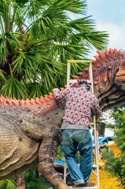 PATTAYA, THAILAND-Aralık 30. 2018: Ressam, Nong Nooch Tropik Botanik Bahçesi 'ni güzel ve gerçekçi kılmak için büyük dinozor heykeli veya heykelini boyamak ve dekore etmek üzere merdivenin üzerinde duruyor.