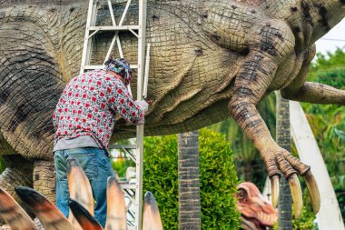 PATTAYA, THAILAND-Aralık 30. 2018: Ressam, Nong Nooch Tropik Botanik Bahçesi 'ni güzel ve gerçekçi kılmak için büyük dinozor heykeli veya heykelini boyamak ve dekore etmek üzere merdivenin üzerinde duruyor.