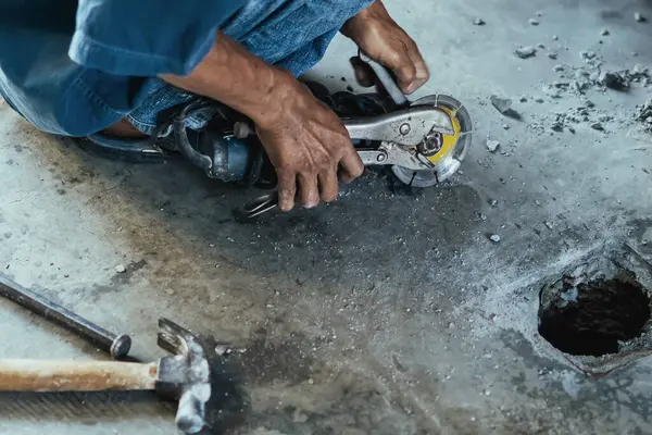 Su tesisatı bakım servisi evdeki kanalizasyon kanallarını değiştirmek için açılı öğütücü kullanıyor. Yaşlı adam kanalizasyon sisteminin lağım kapağını değiştirip onarıyor. Tuvalet drenaj sisteminin bakımı