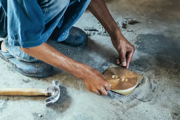 Su hizmetleri bakım servisinin yaşlı çalışanı evdeki kanalizasyon kanallarını değiştiriyor. Yaşlı adamın elleri kanalizasyon sisteminin lağım kapağını değiştirip onarıyor. Tuvalet drenaj sisteminin bakımı.