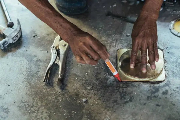 Su hizmetleri bakım servisinin yaşlı çalışanı evdeki kanalizasyon kanallarını değiştiriyor. Yaşlı adamın elleri kanalizasyon sisteminin lağım kapağını değiştirip onarıyor. Tuvalet drenaj sisteminin bakımı.