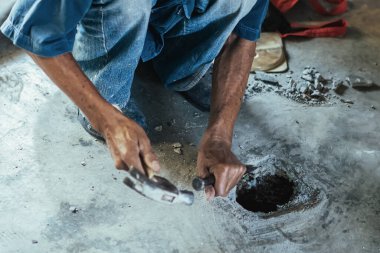 Su hizmetleri bakım servisinin yaşlı çalışanı evdeki kanalizasyon kanallarını değiştiriyor. Yaşlı adamın elleri kanalizasyon sisteminin lağım kapağını değiştirip onarıyor. Tuvalet drenaj sisteminin bakımı.