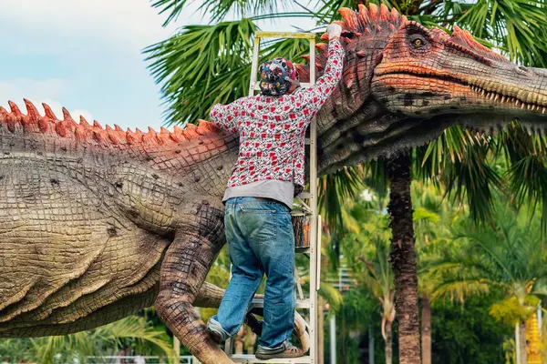 PATTAYA, THAILAND-Aralık 30. 2018: Ressam, Nong Nooch Tropik Botanik Bahçesi 'ni güzel ve gerçekçi kılmak için büyük dinozor heykeli veya heykelini boyamak ve dekore etmek üzere merdivenin üzerinde duruyor.