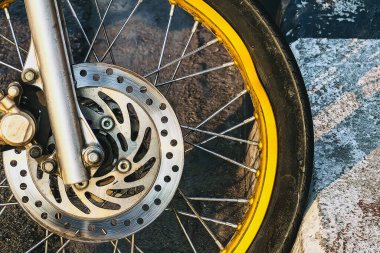 Motosikletin ön tekerleği yolun kenarına düşmüş ve eğilmiş. Çemberi bükülmüş motorsiklet tekerleği hasar görmüş. Goolden alaşımlı motosiklet tekerleği hasar görmüş. Eğri ya da büğrü motosiklet ya da motosiklet kenarı.