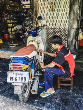 KANCHANABURI, THAILAND - 12023 ARALIK: Motosiklet tamircisi ve bozuk para aküsü motorsiklet garajında motorsikletle yeni aküye doğru azalıyor. Onarım ve bakım motosiklet kavramları.