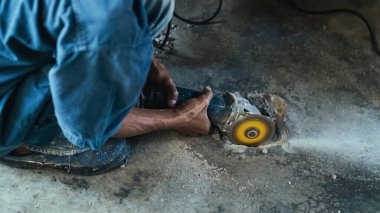Su tesisatı bakım servisi evdeki kanalizasyon kanallarını değiştirmek için açılı öğütücü kullanıyor. Yaşlı adam kanalizasyon sisteminin lağım kapağını değiştirip onarıyor. Tuvalet drenaj sisteminin bakımı