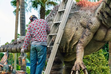 PATTAYA, THAILAND-Aralık 30. 2018: Ressam, Nong Nooch Tropik Botanik Bahçesi 'ni güzel ve gerçekçi kılmak için büyük dinozor heykeli veya heykelini boyamak ve dekore etmek üzere merdivenin üzerinde duruyor.