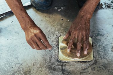 Su hizmetleri bakım servisinin yaşlı çalışanı evdeki kanalizasyon kanallarını değiştiriyor. Yaşlı adamın elleri kanalizasyon sisteminin lağım kapağını değiştirip onarıyor. Tuvalet drenaj sisteminin bakımı.