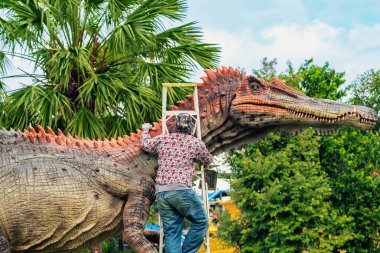 PATTAYA, THAILAND-Aralık 30. 2018: Ressam, Nong Nooch Tropik Botanik Bahçesi 'ni güzel ve gerçekçi kılmak için büyük dinozor heykeli veya heykelini boyamak ve dekore etmek üzere merdivenin üzerinde duruyor.