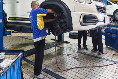 KANCHANABURI, THAILAND - 25 Mayıs 2024: Asyalı araba tamircisi veya tamircisi ön teker çekiş arabasında disk frenini ve araba CV Axles 'ın yerini kontrol ediyor. Dao Tharua Mağazası 'na tekerlek merkezi yerleştirildi.