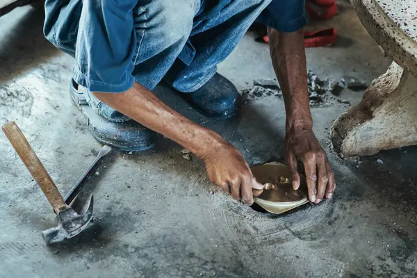 Su hizmetleri bakım servisinin yaşlı çalışanı evdeki kanalizasyon kanallarını değiştiriyor. Yaşlı adamın elleri kanalizasyon sisteminin lağım kapağını değiştirip onarıyor. Tuvalet drenaj sisteminin bakımı.