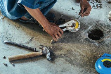 Su tesisatı bakım servisi evdeki kanalizasyon kanallarını değiştirmek için açılı öğütücü kullanıyor. Yaşlı adam kanalizasyon sisteminin lağım kapağını değiştirip onarıyor. Tuvalet drenaj sisteminin bakımı