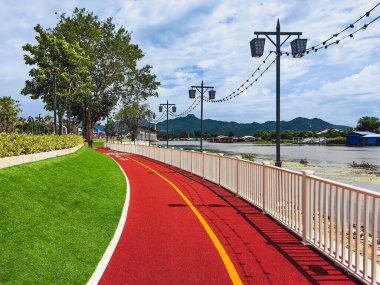 Halka açık güzel yürüyüş yolu manzarası ya da nehir kenarındaki suni çimlerden yapılmış koşu pisti insanların egzersiz yapması, güzel manzaranın tadını çıkarması ve Kanchanaburi, Tayland 'da temiz hava soluması için..