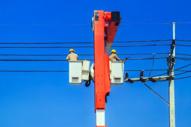 Elektrikçiler ya da kova patlatıcısının mühendisi elektrik sistemini elektrik direğine birçok kablo hattıyla yüklemek için çalışıyor. Elektrikçiler elektrik direğindeki kabloyu tamir ediyorlar. Yüksek voltaj güç hattı onarımı