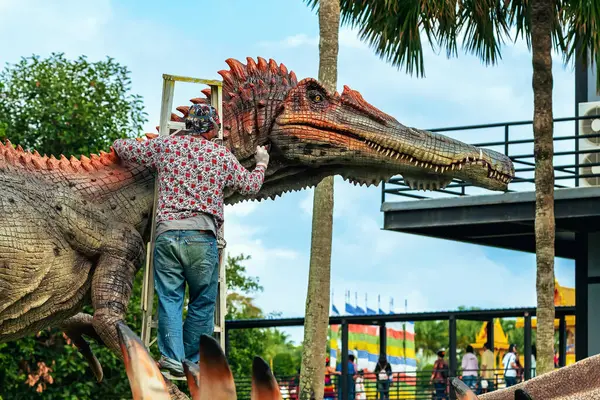 PATTAYA, THAILAND-Aralık 30. 2018: Ressam, Nong Nooch Tropik Botanik Bahçesi 'ni güzel ve gerçekçi kılmak için büyük dinozor heykeli veya heykelini boyamak ve dekore etmek üzere merdivenin üzerinde duruyor.