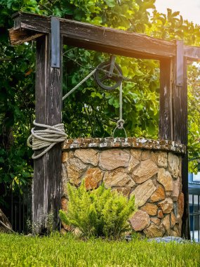 Taş ve tekerlek makara ile yapılmış güzel artezyen metal kova ve halatla huzurlu bahçe atmosferinde. Kırsal alandaki Retro Stone Kuyusu. Antika eşyalarla bahçe dekorasyonu.