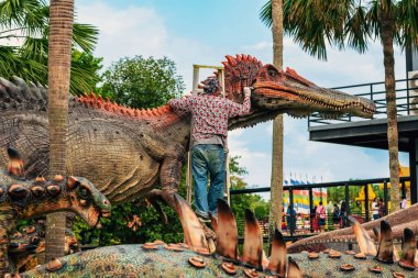 PATTAYA, THAILAND-Aralık 30. 2018: Ressam, Nong Nooch Tropik Botanik Bahçesi 'ni güzel ve gerçekçi kılmak için büyük dinozor heykeli veya heykelini boyamak ve dekore etmek üzere merdivenin üzerinde duruyor.