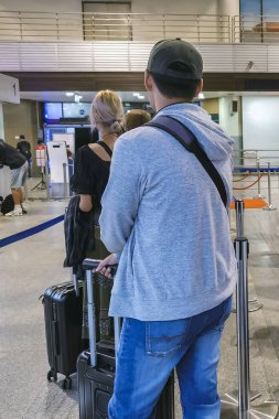 Havaalanı terminalinde bagaj kuyruğunda bekleyen insanlar. Kayıt alanında sırada bekleyen erkek turistler var. Uçuşları kontrol etmek için kuyrukta bekleyen erkek yolcular seyahat yolculuğuna giderler..