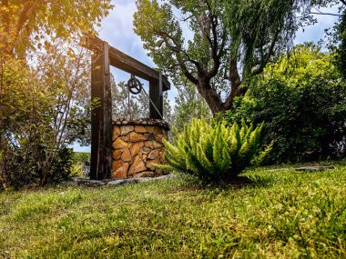 Taş ve tekerlek makara ile yapılmış güzel artezyen metal kova ve halatla huzurlu bahçe atmosferinde. Kırsal alandaki Retro Stone Kuyusu. Antika eşyalarla bahçe dekorasyonu.