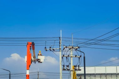 Elektrikçiler ya da kova patlatıcısının mühendisi elektrik sistemini elektrik direğine birçok kablo hattıyla yüklemek için çalışıyor. Elektrikçiler elektrik direğindeki kabloyu tamir ediyorlar. Yüksek voltaj güç hattı onarımı