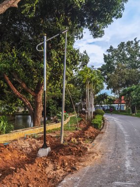 Kamu parkında alternatif enerji kaynağı olarak güneş enerjisini kullanmak için yeni güneş sokak lambaları kurmak için çukur kazmak. Yol boyunca ayakta duran yeni güneş pili elektrik direğinin görüntüsü