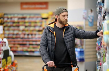 Sakallı beyaz bir adam süpermarkette hijyen ürünleriyle ilgileniyor.