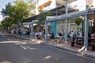 Brisbane, Queensland, Avustralya - Ağustos 2022: Pazar sabahı kahvaltısı için bir açık kafe kaldırımında yemek yiyen insanlar.