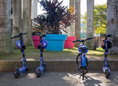 Brisbane, Queensland, Avustralya - Ağustos 2022: Konsey scooterları açık hava parkındaki büyük ot fabrikalarının önüne park edildi.