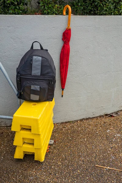 Camera bag and red umbrella on a yellow step stool against a grey wall