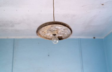Ampul, eski ve ihmal edilmiş bir cazibe katan aşınmış bir armatürüne bağlı..