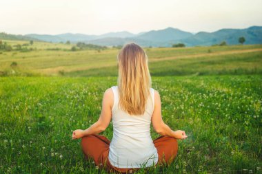 Dağın tepesindeki yeşil çimlerde yoga yapan kadın gün batımında güzel manzaralı.