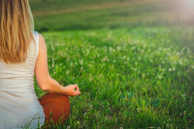Woman doing yoga on the green grass on the top of the mountain with beautiful view at sunset