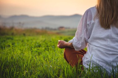 Dağın tepesindeki yeşil çimlerde yoga yapan kadın gün batımında güzel manzaralı.