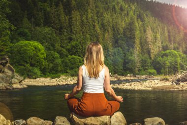 Dağın tepesindeki yeşil çimlerde yoga yapan kadın gün batımında güzel manzaralı.